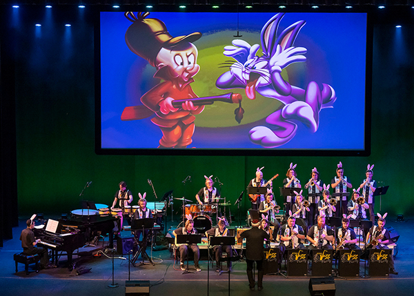 The ETSU Jazz Ensemble performs on stage in front of a giant screen featuring a picture of Bugs Bunny and Elmer Fudd. 