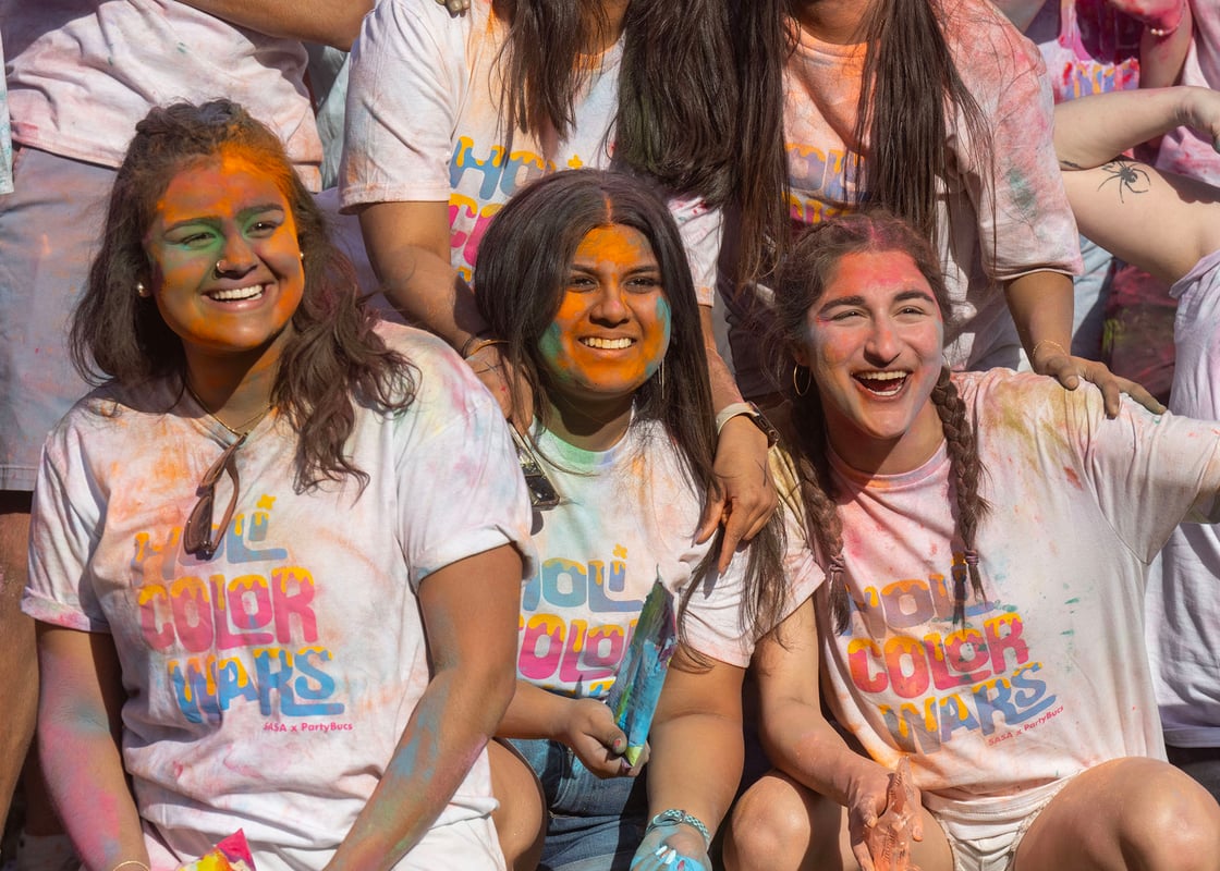 Smiling students covered in colorful powders and wearing a t-shirt that says 