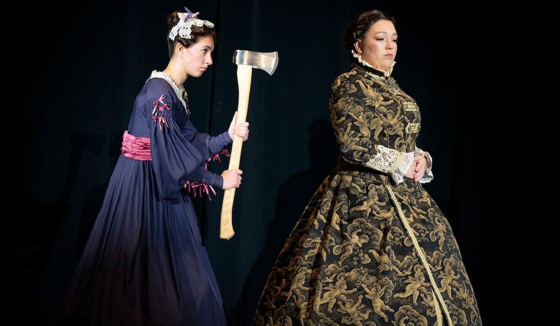 Two women wearing Victorian-style dress. It appears to be night and one woman is stalking the other with an ax. 