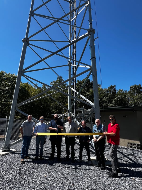 A group of people cut a gold ribbon in front of a radio tower