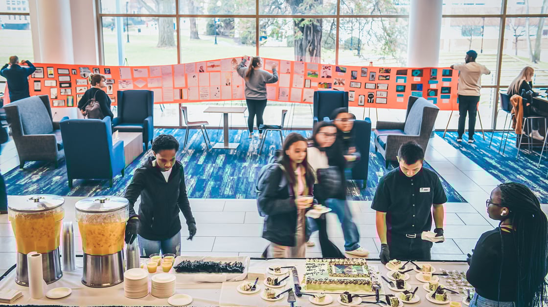 Students gather around refreshments in the D.P. Culp Student Center offered in honor of Martin Luther King, Jr. Day. In the background, others hang artwork celebrating the legacy of Dr. King. 
