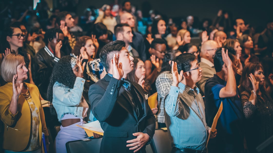 Hundreds of individuals raise their hand to take an oath of citizenship