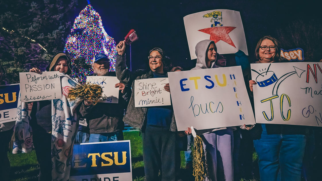 Supporters hold signs congratulating the Marching Bucs and wishing them well as they prepare to board buses headed to NYC